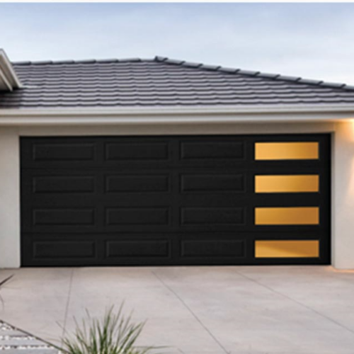 A modern garage door with a dark finish and three horizontal, yellow-lit windows on the right side. The surrounding area features a light-colored driveway, exterior walls, and subtle landscaping with a plant in the foreground.