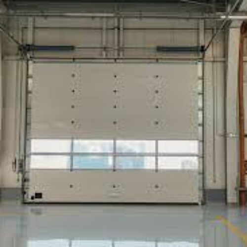 An industrial garage with three large overhead doors. The door panels are white with rows of windows near the bottom. The garage floor is shiny and clean, reflecting ambient light. Steel beams and mechanical components are visible above the doors.